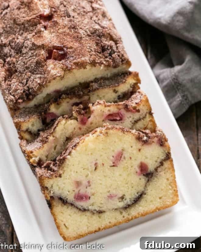 A freshly baked loaf of Cinnamon Swirl Rhubarb Bread on a pristine white platter, showcasing its golden crust and delicious texture.
