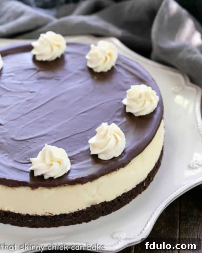 Close view of half of a Baileys cheesecake on a white cake plate, showing distinct layers of brownie, cheesecake, and ganache.