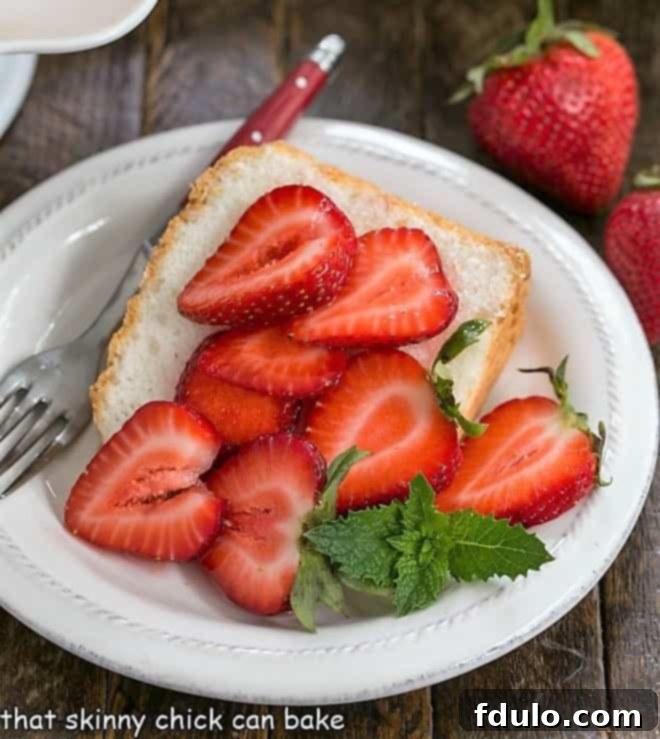 Slice of angel food cake on a white plate topped with berries