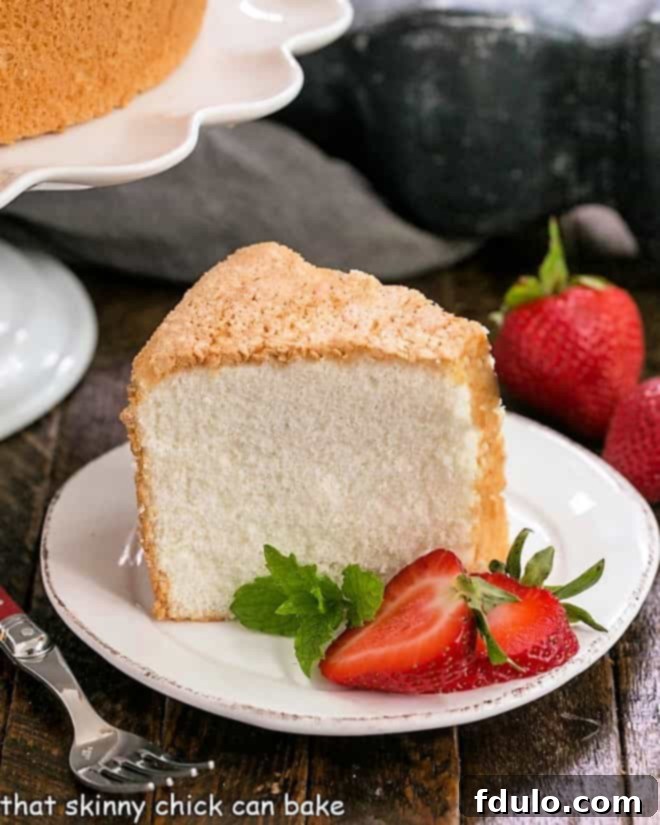 Slice of angel food cake on a white dessert plate with sliced strawberries and mink