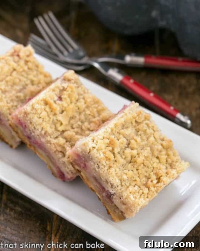 Close-up of golden brown Streusel Topped Rhubarb Bars on a white tray, showcasing the crumbly topping and vibrant pink filling.