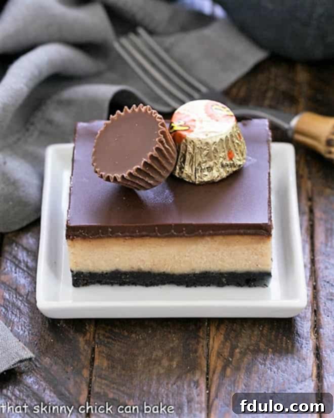 Close-up of a layered peanut butter cheesecake bar, topped with two mini peanut butter cups, showing the rich textures.