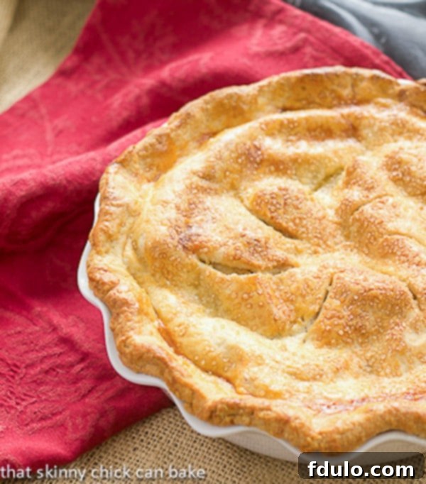 Classic Apple Pie - Sweet, cinnamon spiced apples in a flaky pastry crust A stunning, golden-brown Classic Apple Pie nestled in a ruffled white ceramic pie plate, ready to be served and enjoyed.