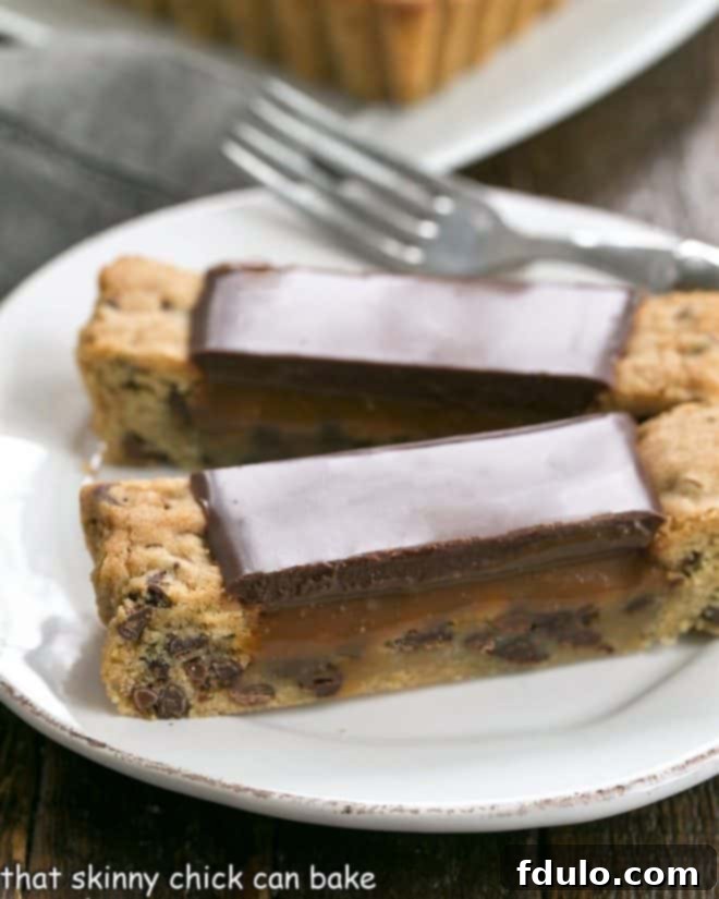 Two slices of chocolate chip cookie tart on a white plate with a fork, showcasing layers of cookie, caramel, and chocolate