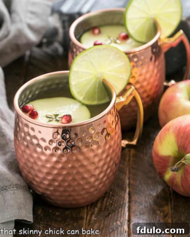 Cider Mules in copper mugs with lime and apple garnishes, showcasing a festive fall cocktail.