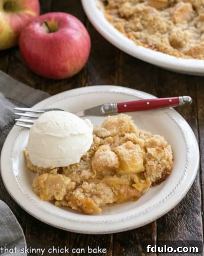 A close-up shot of a serving of Apple Crumble with Custard, showing the luscious filling and crispy topping, with a scoop of vanilla ice cream on a white dessert plate.