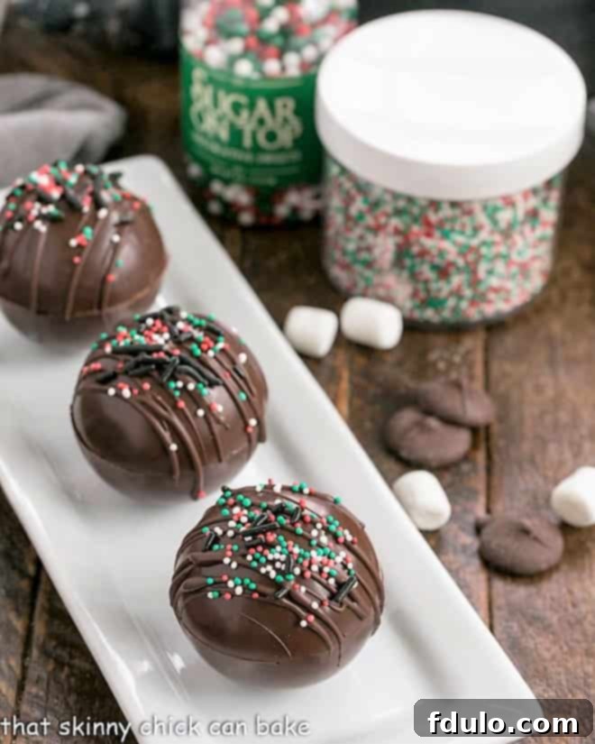 3 hot chocolate bombs on a white tray with sprinkles, marshmallows and chocolate melts, depicting the various components.