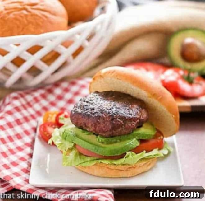 Two beautifully presented California Burgers on a white plate, garnished with fresh lettuce, tomato, and a side of avocado slices.