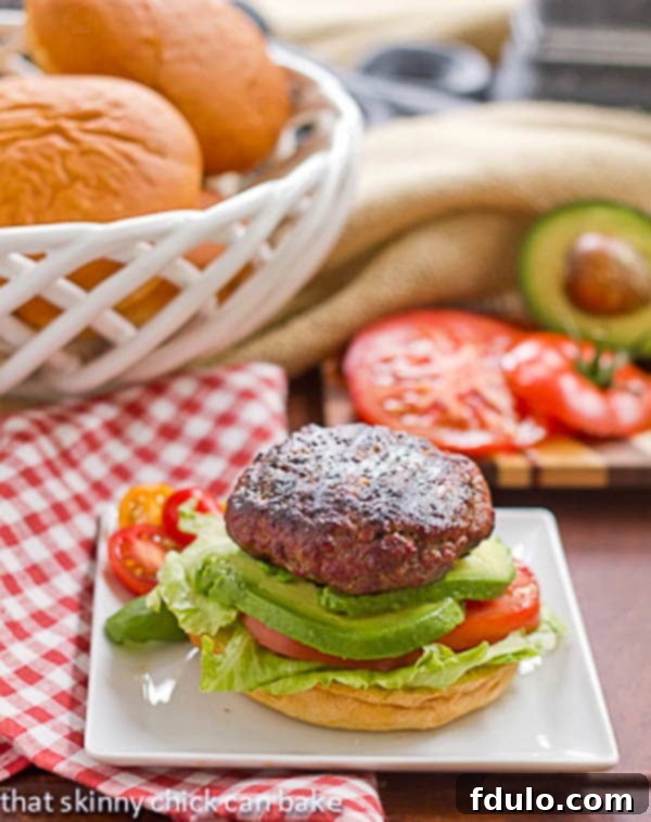 A close-up of a California Burger on a white plate with a red and white checked napkin, showcasing the fresh toppings and perfectly cooked patty.