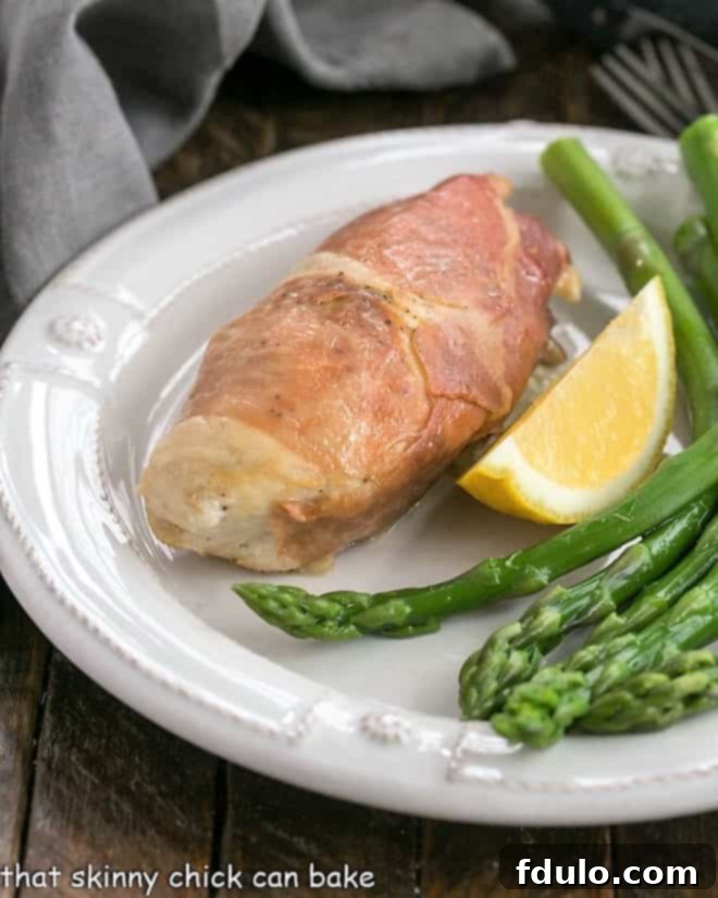Prosciutto Wrapped Chicken with Boursin - Chicken breasts stuffed with creamy herbed Boursin cheese and wrapped in salty Prosciutto ham. An elegant entree that's easy to prepare! A perfectly cooked Boursin Stuffed Chicken Breast on a white plate, garnished with a vibrant lemon wedge and fresh asparagus spears, showcasing its golden-brown exterior and inviting presentation.