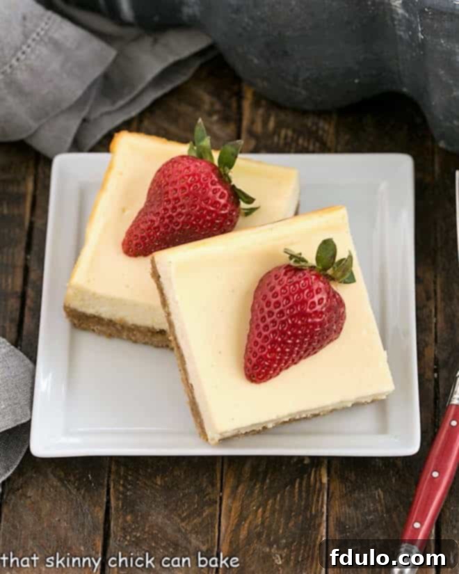 Overhead view of 2 vanilla cheesecake bars topped with strawberry halves on a square white plate
