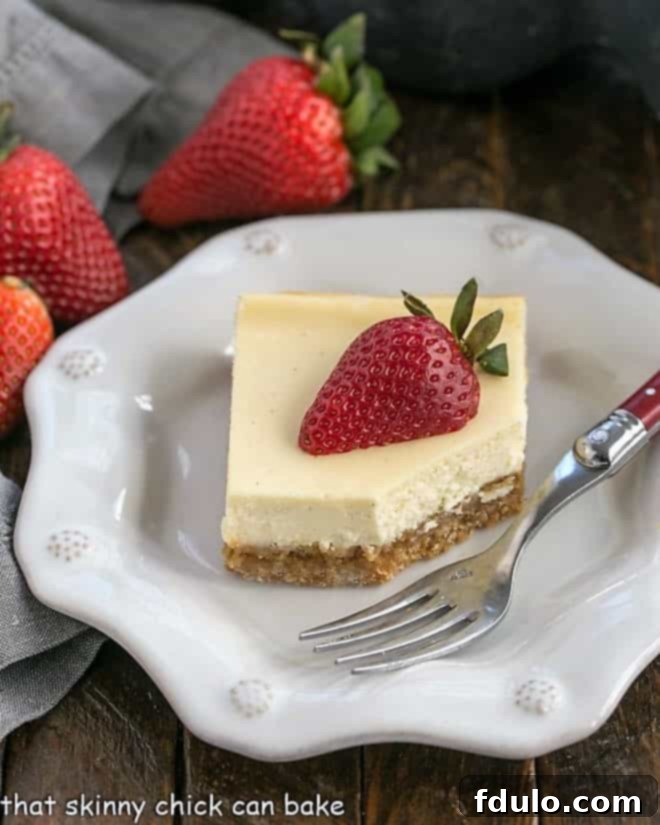 One cheesecake bar topped with a half strawberry on a decorative white plate with a fork