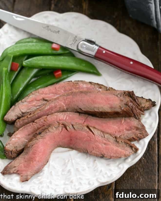 Overhead view of perfectly grilled and sliced flank steak, served with vibrant sugar snap peas and a red-handled knife.