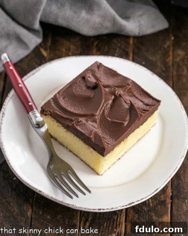 Sunshine Yellow Cake with Chocolatey Dream Frosting 2 A delectable square of moist one-layer yellow cake, generously slathered with rich chocolate frosting, served on a pristine white dessert plate with an elegant red-handled fork.
