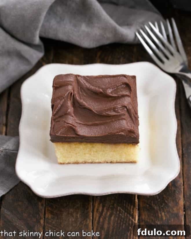 Sunshine Yellow Cake with Chocolatey Dream Frosting 3 An overhead shot showcasing a perfectly cut square of moist yellow snack cake, crowned with smooth chocolate frosting, resting on a clean white dessert plate.