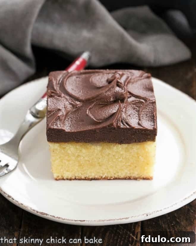 Sunshine Yellow Cake with Chocolatey Dream Frosting 4 A perfectly portioned slice of vibrant yellow snack cake, generously topped with rich chocolate frosting, served on a crisp white plate with a red-handled fork.