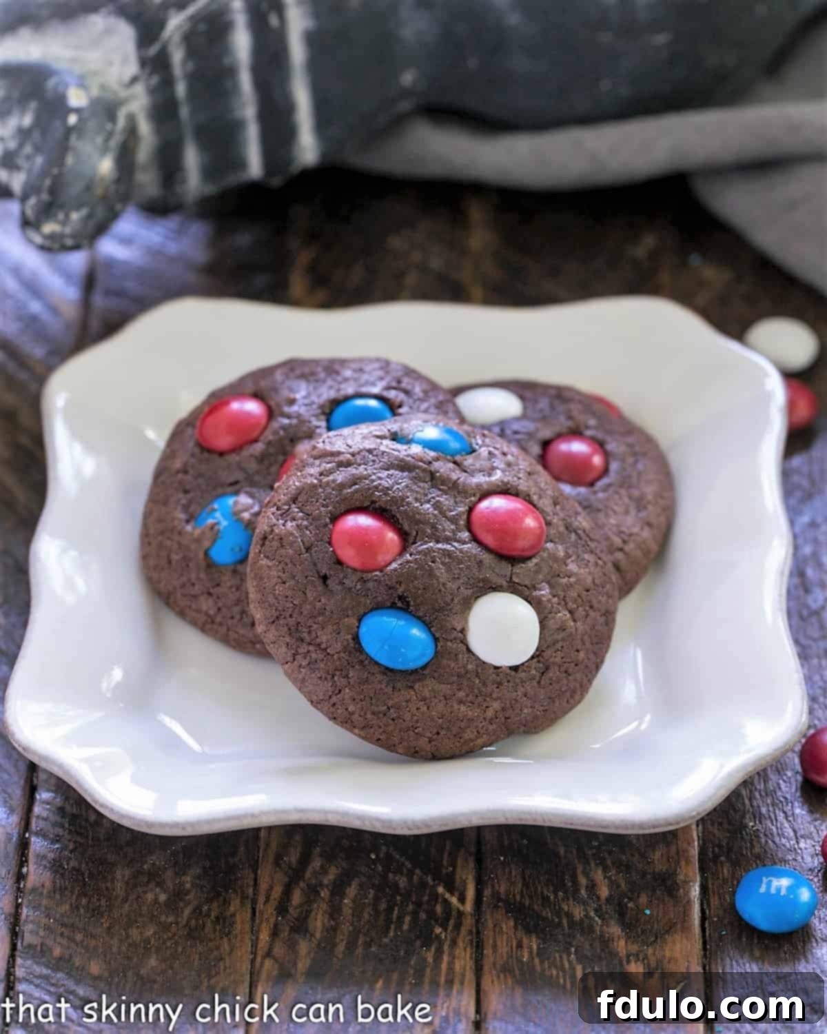 Three perfectly baked 4th of July cookies, adorned with red, white, and blue M&M's, arranged on a pristine white plate, ready for a festive celebration.