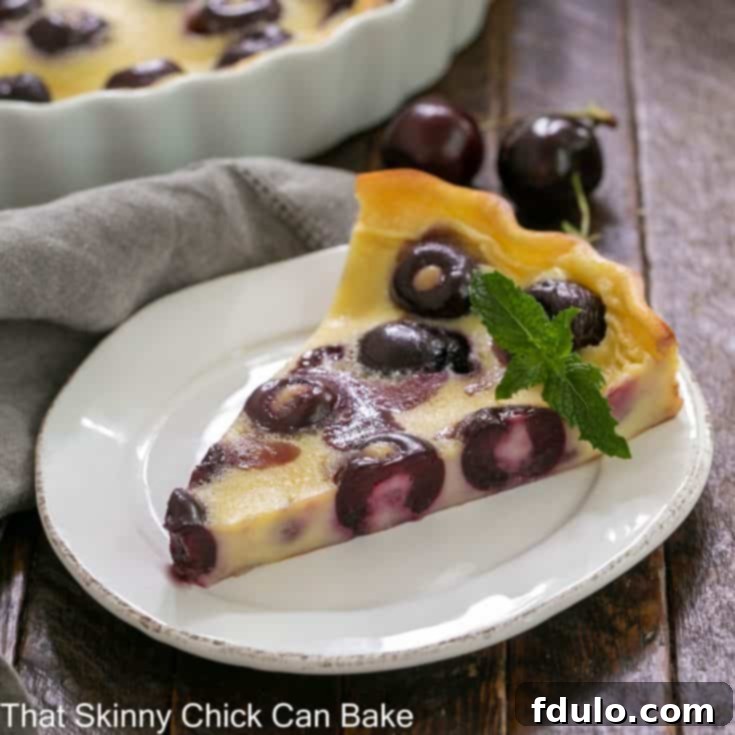 slice of cherry clafoutis on a white plate with a sprig of mint garnish