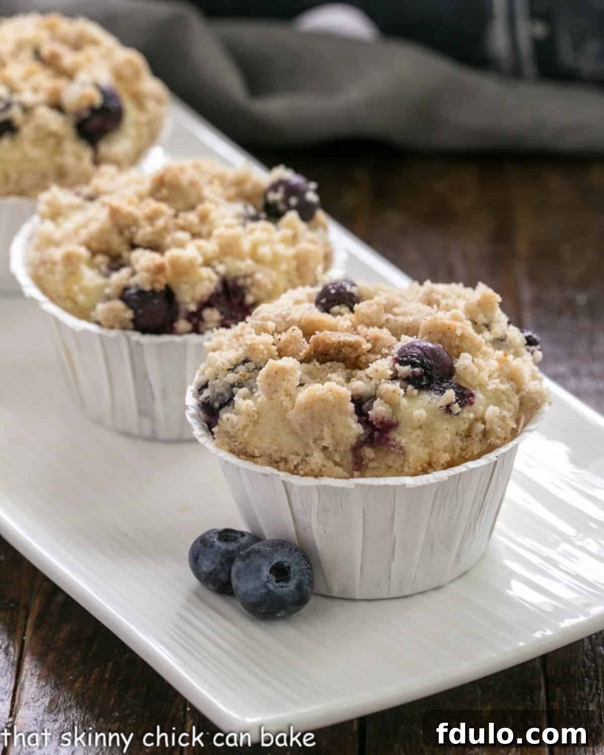 Delightful Blueberry Cream Cheese Muffins arranged beautifully on a pristine white ceramic tray, showcasing their golden streusel topping and juicy blueberry specks.