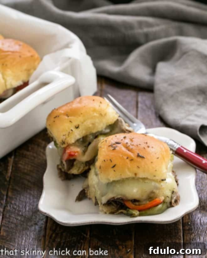 Two golden-brown Philly Cheesesteak Sliders on a white plate with a fork, ready to be enjoyed.