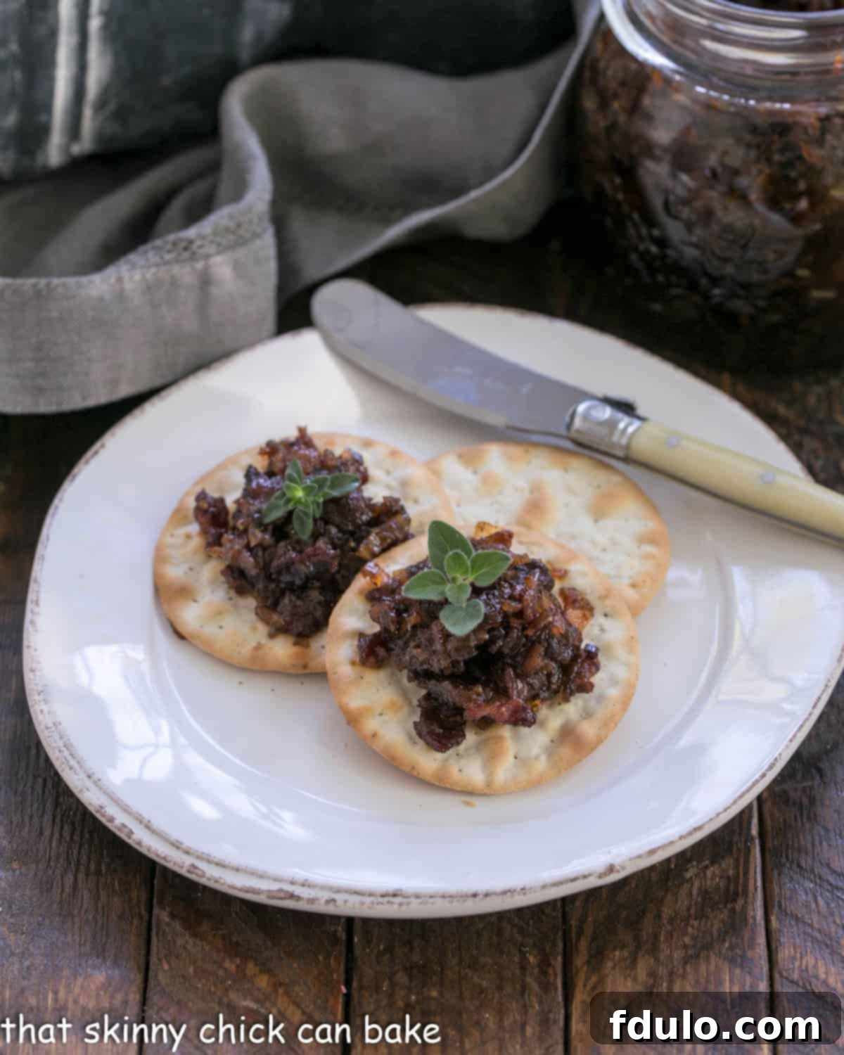 Bacon jam on crackers on a white appetizer plate.