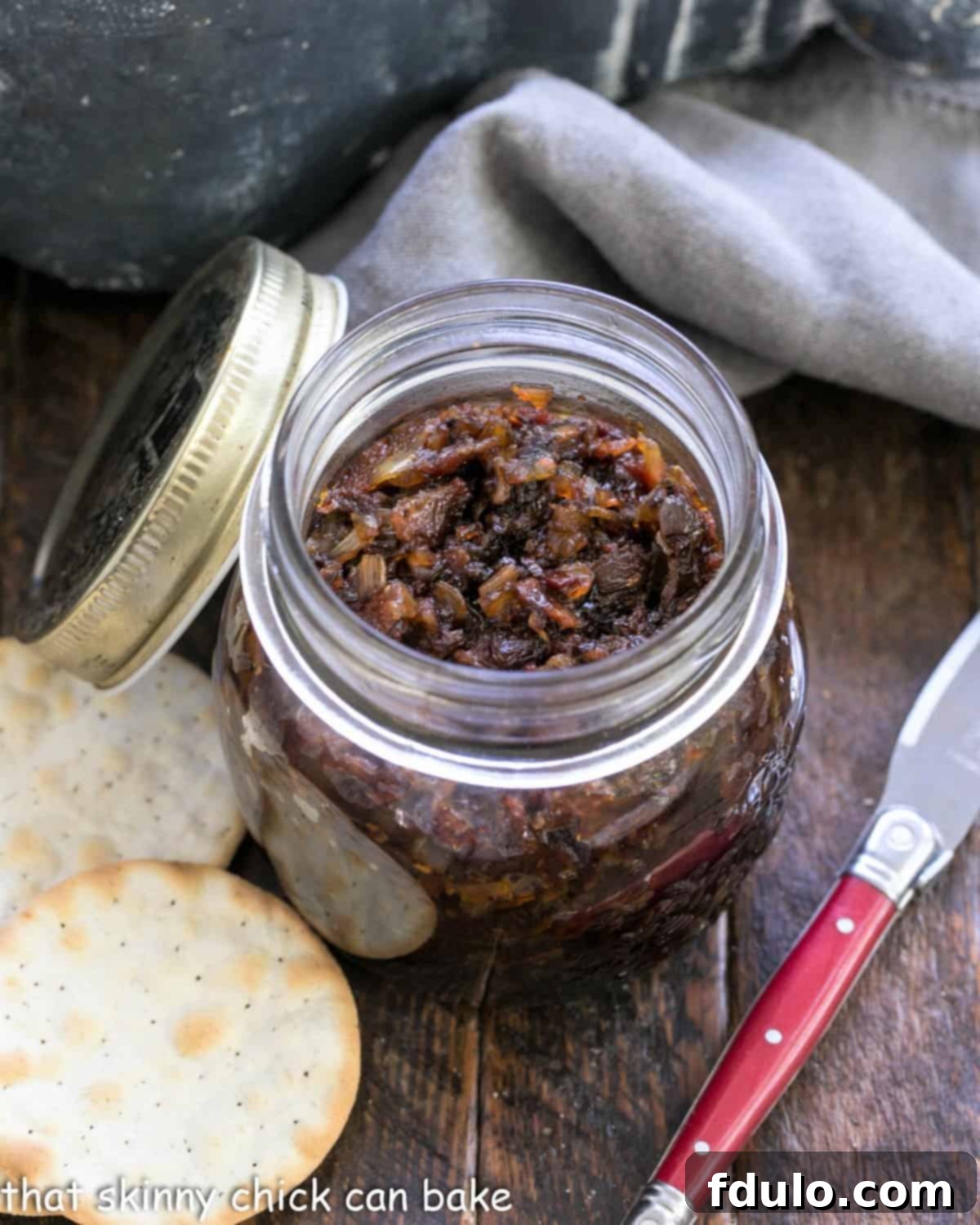 A jar of baon jame with crackers and a red handled knife.