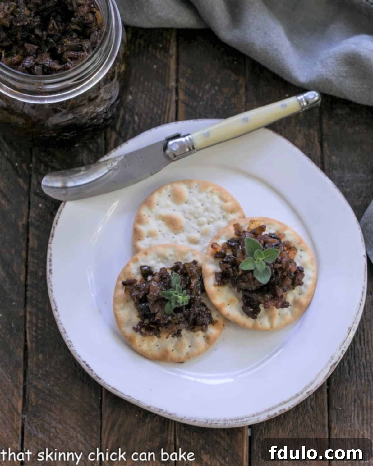 Overhead view of bacon jam on crackers witha ivory handle knife.