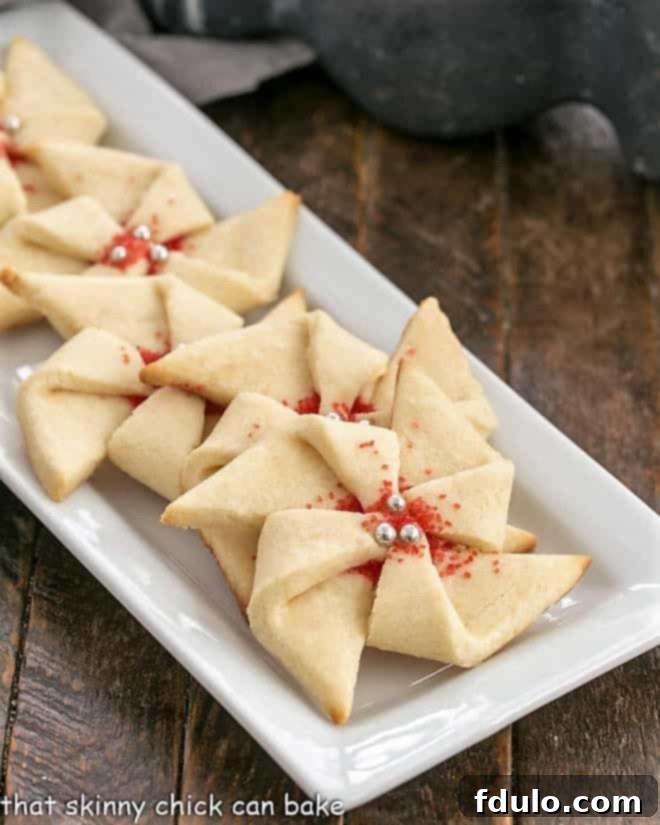 Poinsettia Cookies on a narrow white ceramic tray, showcasing their intricate pinwheel design and vibrant red sprinkles.