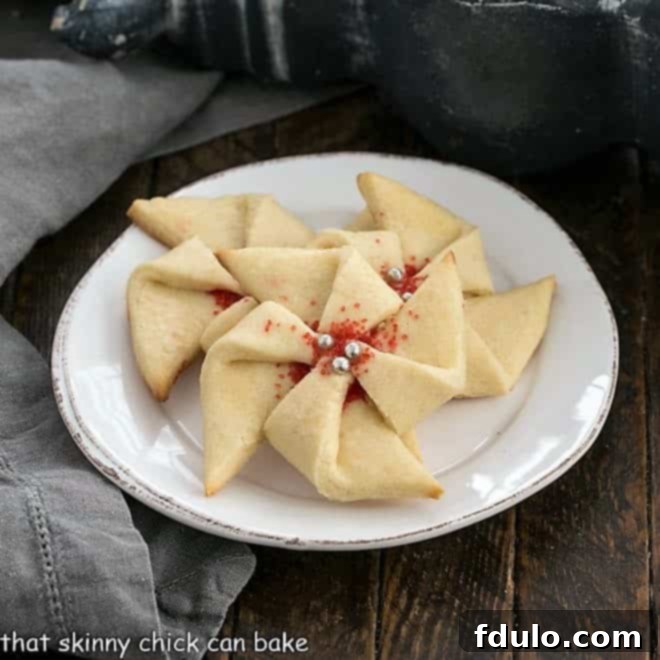 Three Poinsettia Cookies on a small white dessert plate, adorned with red sprinkles.
