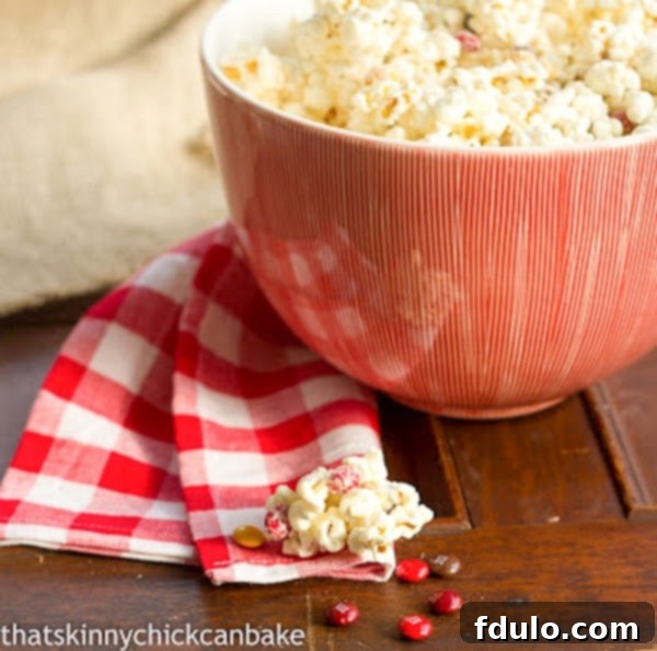 Holiday White Chocolate Popcorn - A Festive Treat for Every Occasion! Holiday White Chocolate Popcorn presented in an elegant red serving bowl, beautifully complemented by a classic red and white checked napkin.