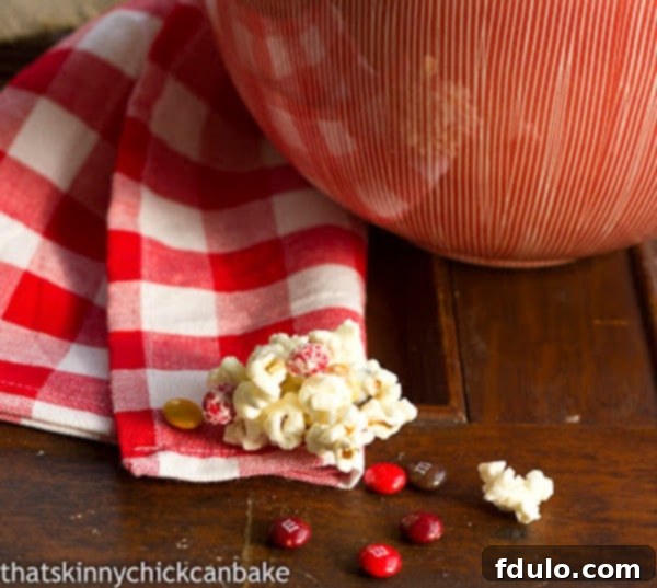Holiday White Chocolate Popcorn - Delicious Candy Popcorn for Gifting and Snacking! Holiday White Chocolate Popcorn with M&M's arranged in front of a serving bowl, highlighting its vibrant appeal.