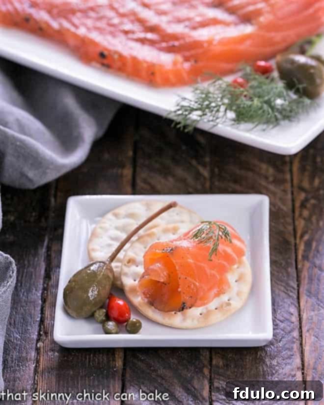 A slice of gravlax on a cracker on a square white plate.