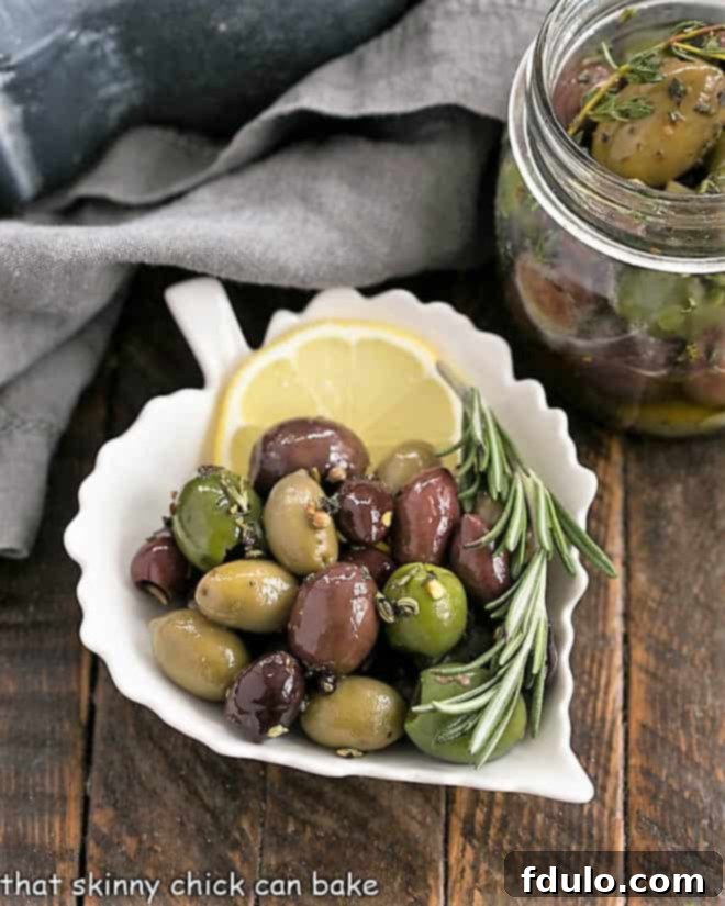 Herbed olives in a ceramic leaf plate with a slice of lemon and rosemary, highlighting the presentation