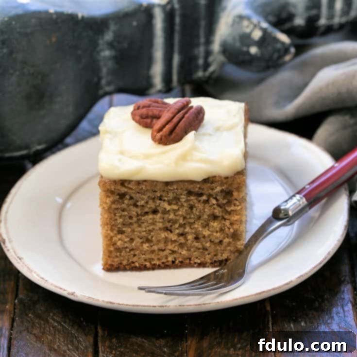 A slice of applesauce spice cake topped with 2 pecan on a round white plate with a red handled fork