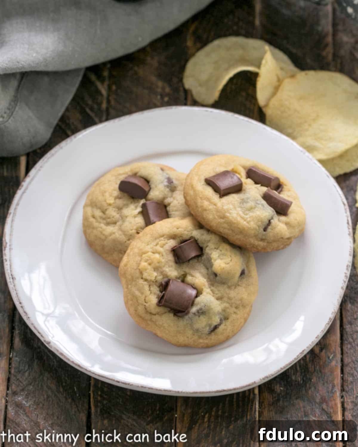 The Salty Sweet Chocolate Crunch Cookie 2 Overhead view of 3 potato chip cookies on a white dessert plate, highlighting their texture and chocolate chunks.