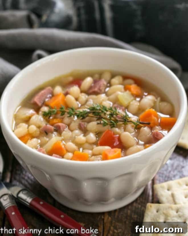 Hearty Navy Bean and Ham Soup 2 A steaming bowl of hearty Navy Bean Soup with crackers and two red-handled spoons on a rustic wooden surface, perfect for a cold evening meal.