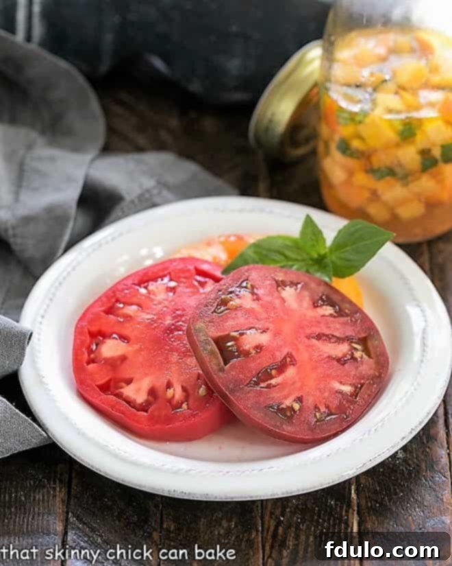 Sliced ripe tomatoes on a small white plate, with a bowl of peach vinaigrette in the soft-focus background, ready for assembly.