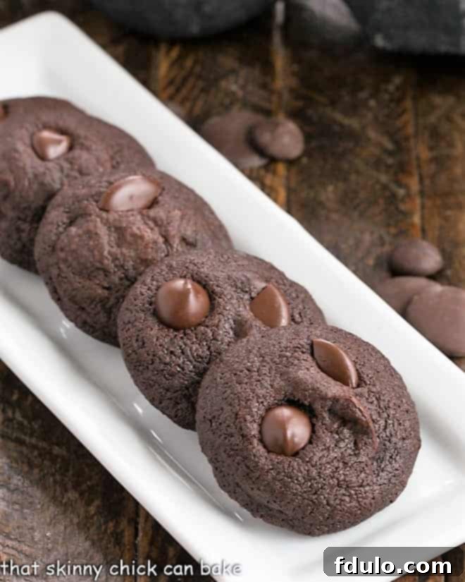 Four perfectly baked bite-sized chocolate cookies arranged on a sleek, narrow white ceramic tray, highlighting their rich color and tempting texture.