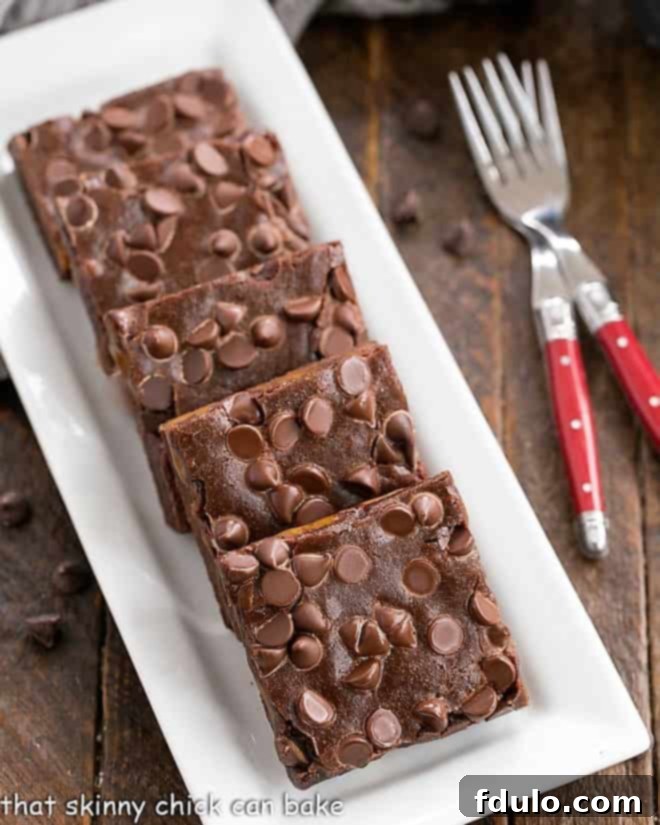 Overhead view of slices Caramel Brownies on a white rectangular tray with a couple of red handled forks, highlighting the rich chocolate and caramel layers.