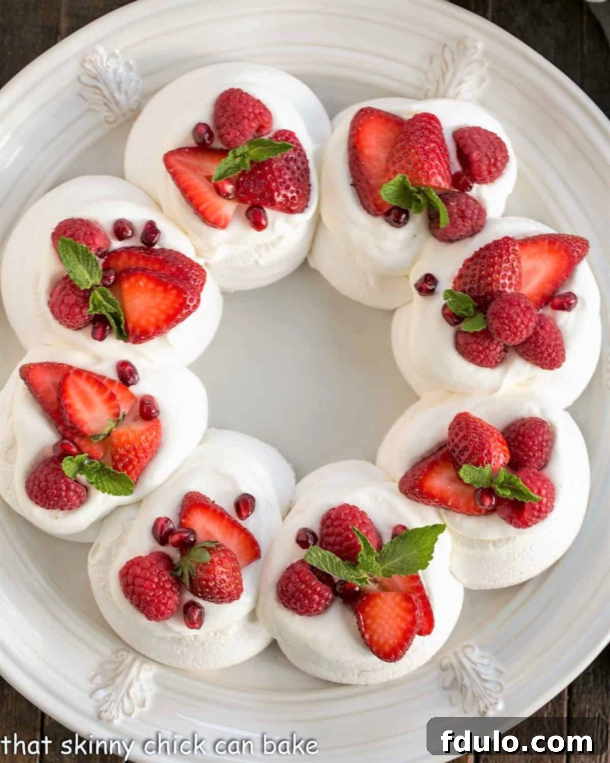 Overhead view of a Christmas Pavlova on a white plate topped with cream, berries and mint, showcasing its festive appeal.