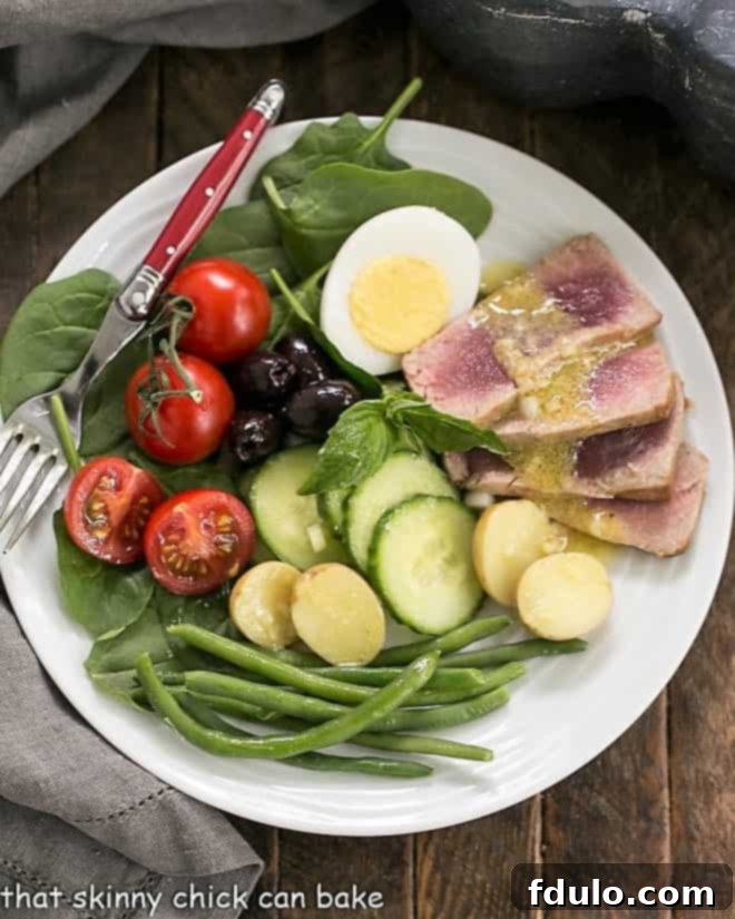 Overhead view of an Ahi Tuna Salade Niçoise on a white plate, showcasing vibrant fresh ingredients and seared tuna.