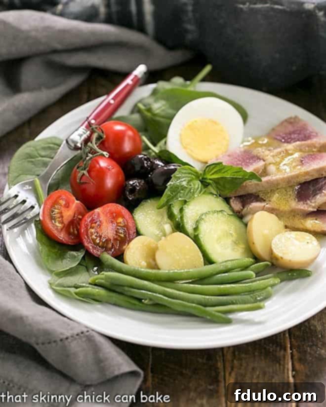 Ahi Tuna Salade Niçoise on a white salad plate with a red handled fork, showing a close-up of the tuna and vegetables.