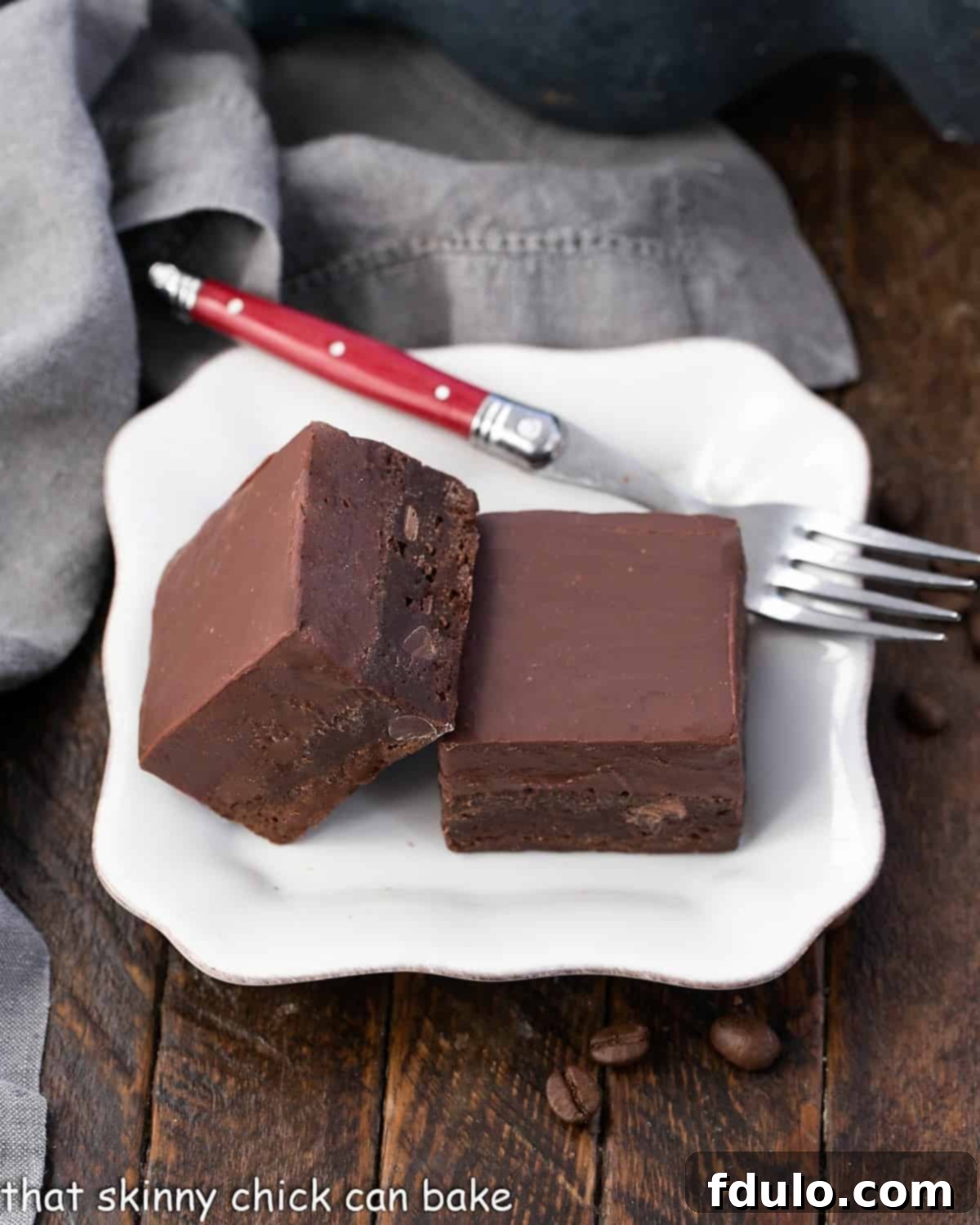 Two kalua fudge topped brownies on a square white plate with a red handle fork.