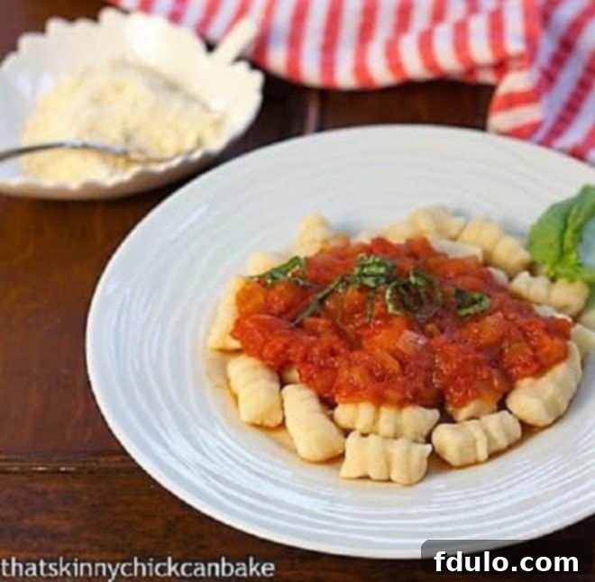 Ricotta Gnocchi topped with marinara and fresh basil on a white dinner plate with a small bowl of Parmesan in the background.